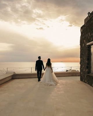 Sposi di spalle sulla terrazza in pietra di Villa Hera, al tramonto sul mare.
