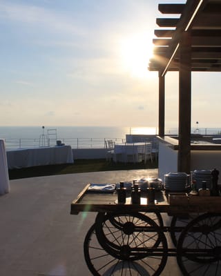 Carretto bar in legno sotto la veranda di Villa Hera, con il mare al tramonto.