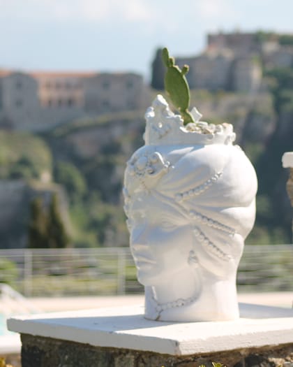Testa di moro in ceramica bianca su un muretto di Villa Hera; sullo sfondo, sfocato, il Castello di Milazzo.