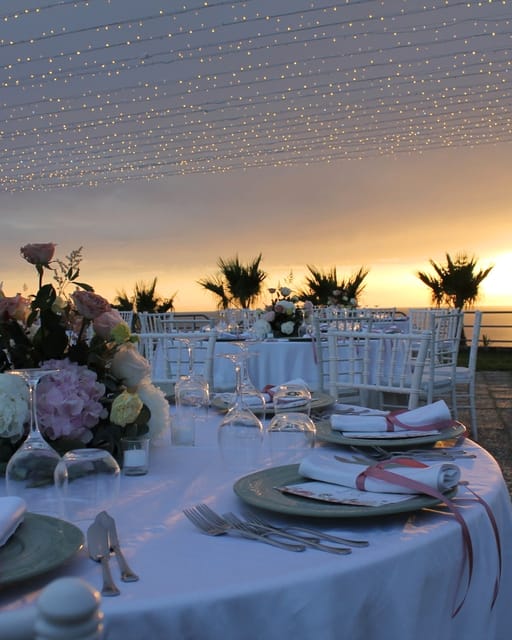 Tavolo apparecchiato con fiori e piatti decorati sulla terrazza, al tramonto.