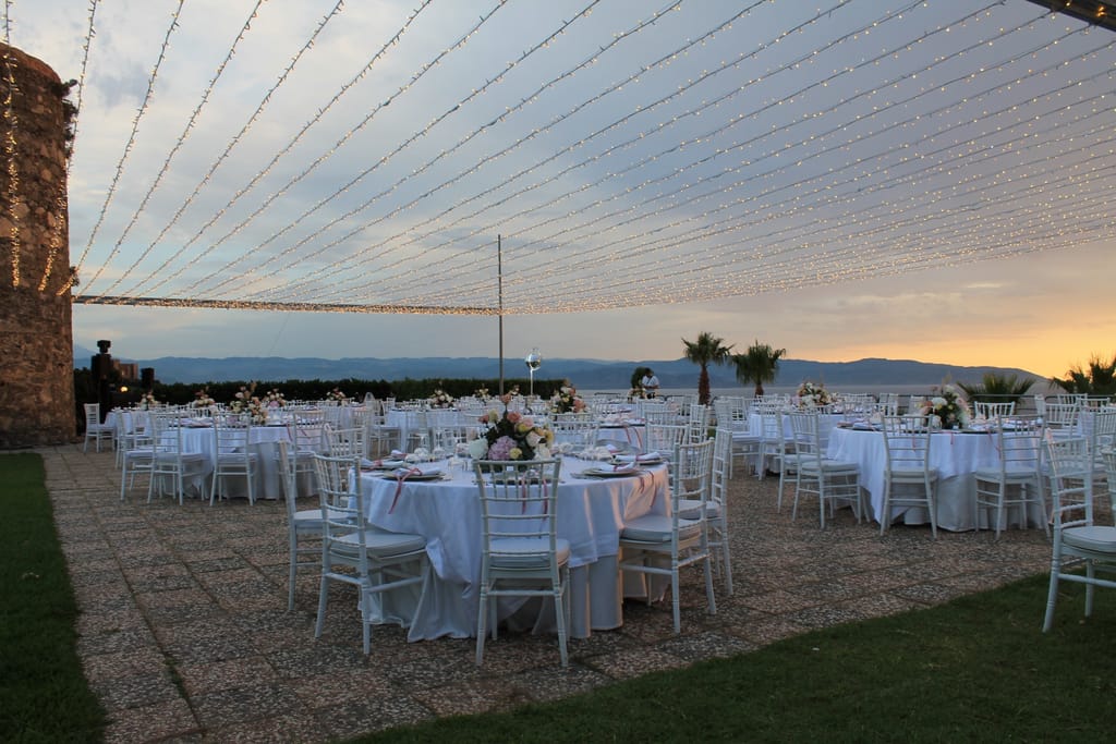 Terrazza di Villa Hera con i tavoli apparecchiati sotto le luci a filo, al tramonto sul mare.