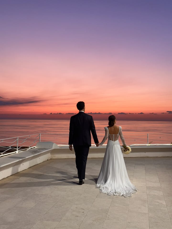 Sposi di spalle sulla terrazza di Villa Hera, mano nella mano, davanti al mare al tramonto.