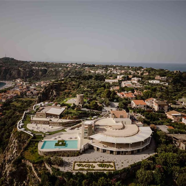 Veduta aerea di Villa Hera di giorno, sul promontorio di Capo Milazzo: la piscina, la Torre Saracena e il mare da entrambi i lati.