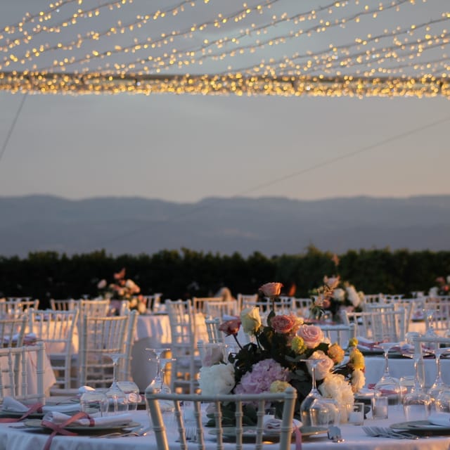 Tavoli con fiori sotto le luci a filo sulla terrazza di Villa Hera.