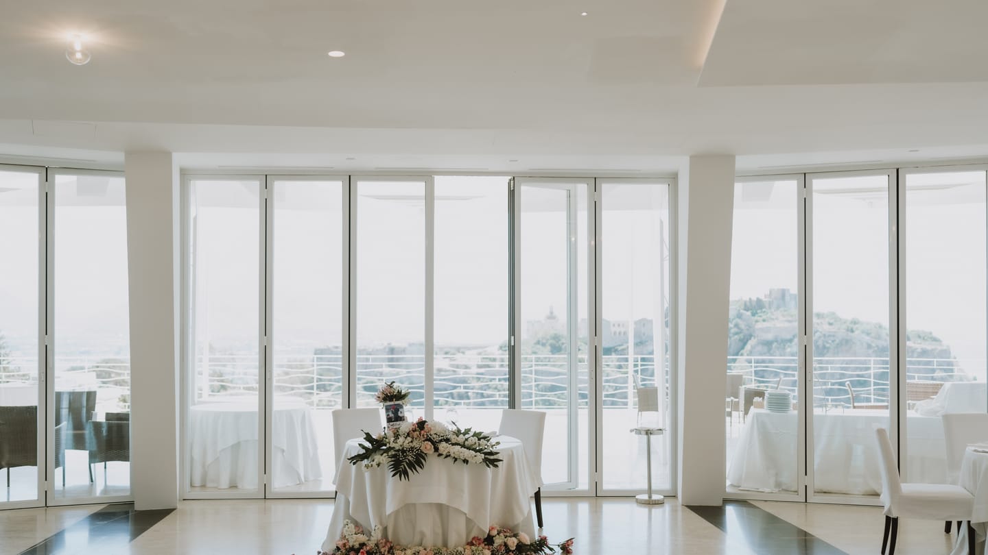 Sala Panoramica di Villa Hera, bianca e luminosa, con grandi vetrate sul Castello di Milazzo.